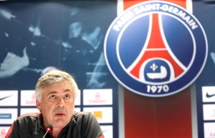 Carlo Ancelotti speaking at a press conference with the Paris Saint-Germain (PSG) club logo visible in the background.