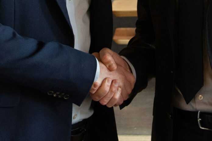 Two business professionals in suits shaking hands, symbolising negotiation, partnership, and trust in sports agency work.