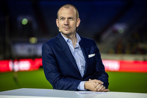 Peer Niclas Naubert, Chief Executive Officer of Bundesliga International, seated at a studio desk in a stadium, wearing a navy blue blazer and speaking into a headset microphone.