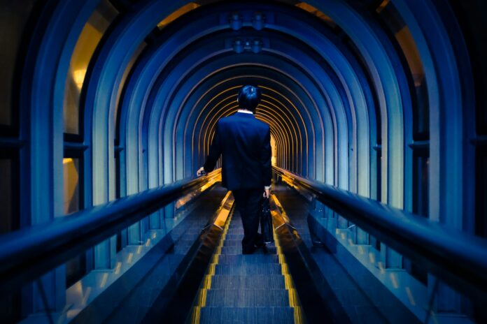 Businessman walking through a modern, arched tunnel with subdued lighting, symbolising discretion and focus in professional negotiations.