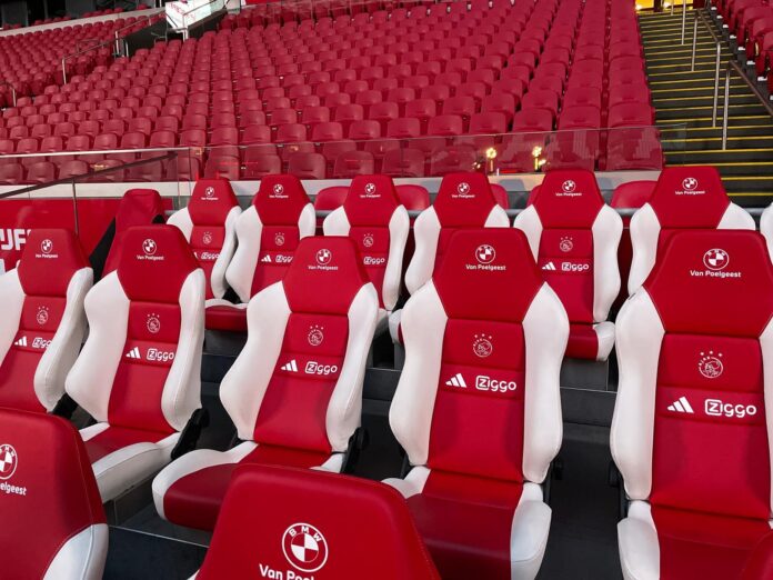 Red and white Ajax substitute bench seats at Johan Cruyff Arena, symbolizing the challenge and opportunity of not starting in football.