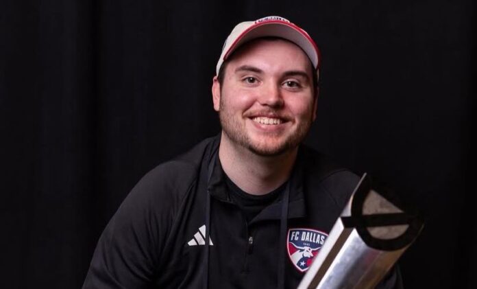 Brandon Hervey, FC Dallas scout, smiling while holding a trophy, wearing FC Dallas team apparel.