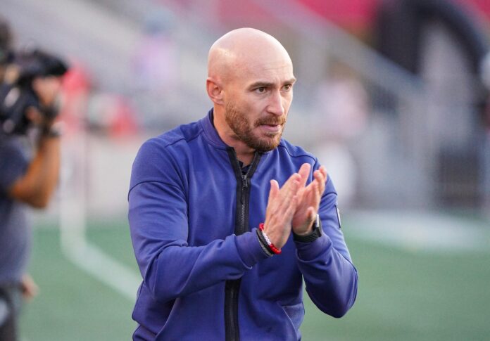 Carlos González, head coach of Atlético Ottawa, applauds his team from the sidelines during a Canadian Premier League match.