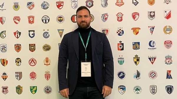 Can Özata standing in front of football club logos at an industry event.