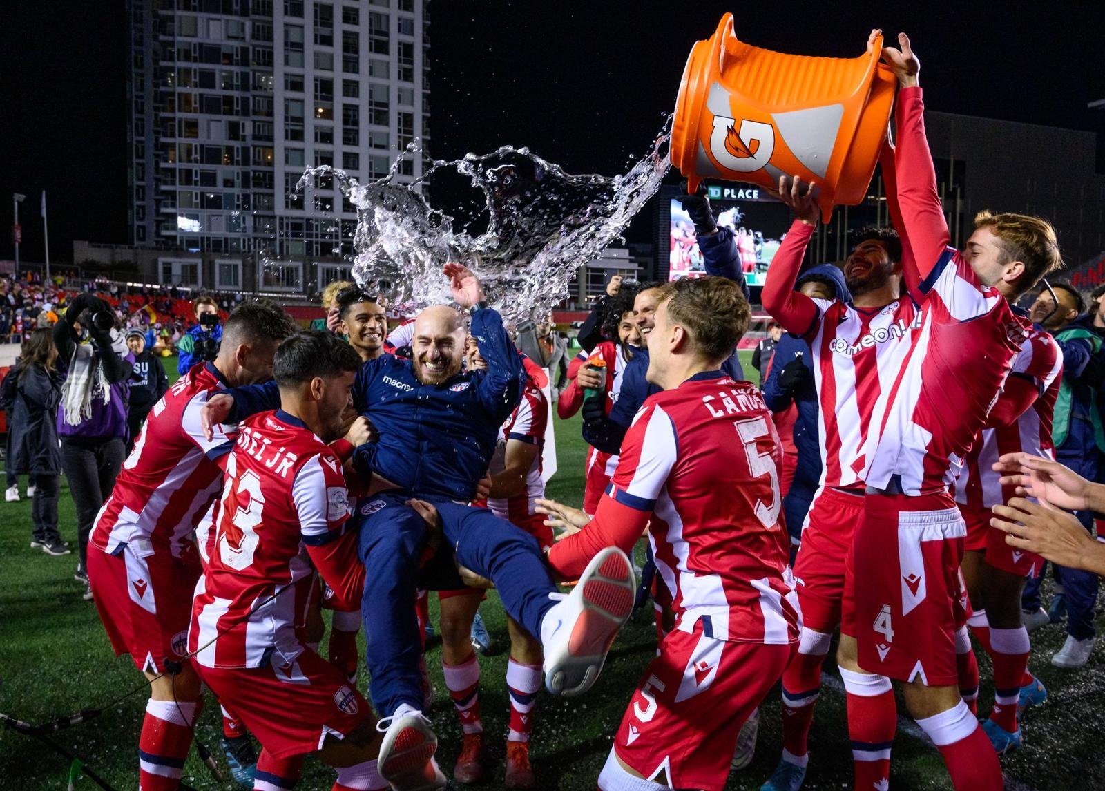 Carlos González celebrates with Atlético Ottawa players, lifted by the team as water is poured over him after a Canadian Premier League victory.