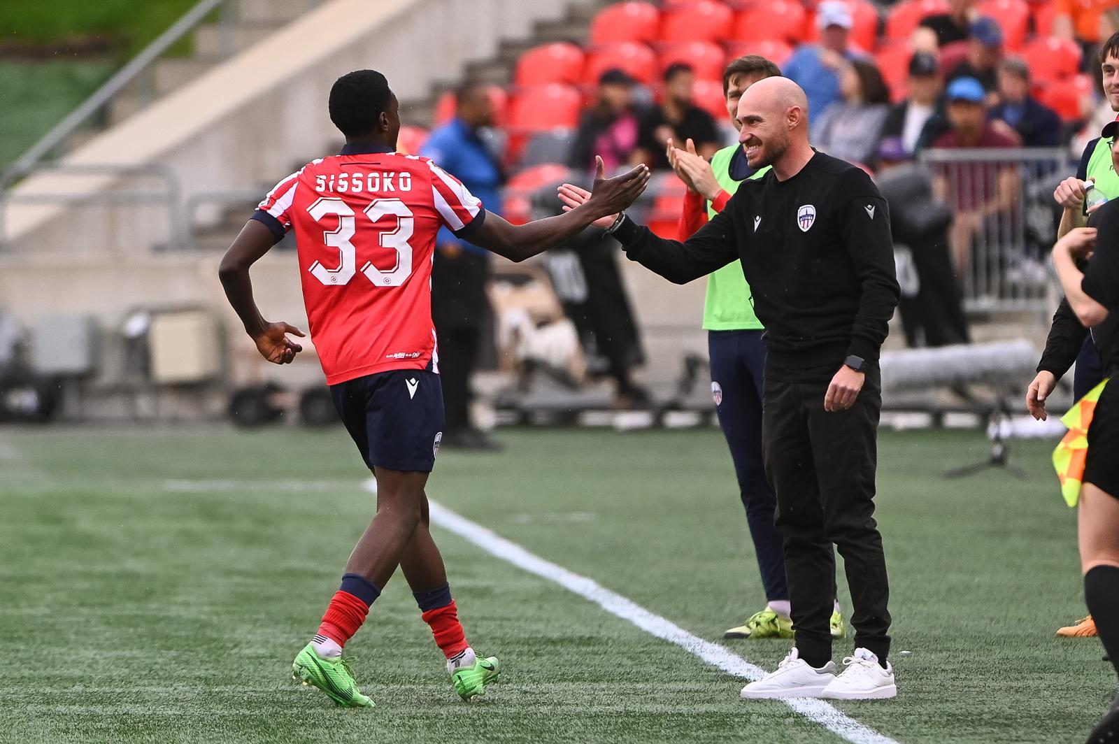 Atlético Ottawa coach Carlos González celebrates with player Aboubacar Sissoko (#33) on the sidelines during a Canadian Premier League match.
