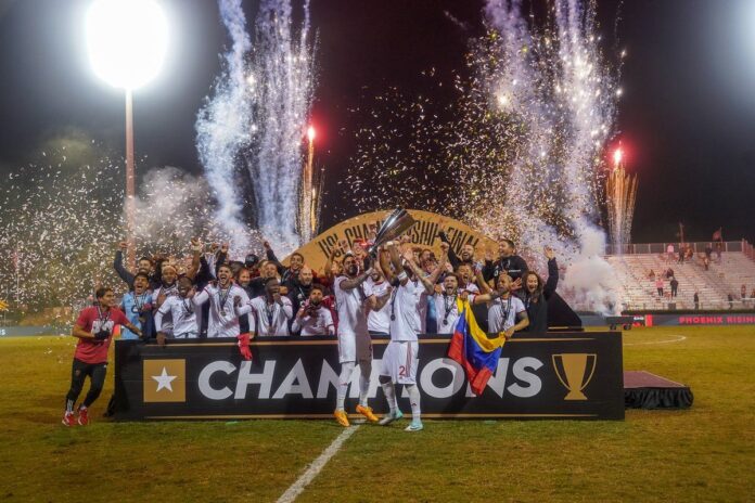 Phoenix Rising players celebrate their 2023 USL Championship victory with the trophy, fireworks, and confetti on the pitch.