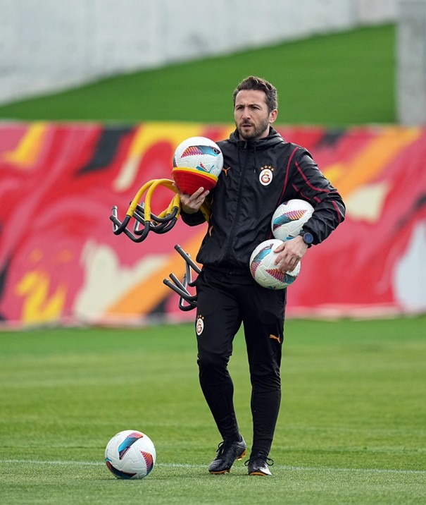 Vural Durmuş carrying training equipment and footballs on the pitch at Galatasaray training ground.