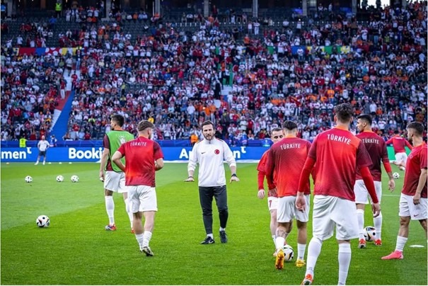 Vural Durmuş leading the Turkish National Team warm-up session on the pitch before a match, with players wearing Türkiye shirts.