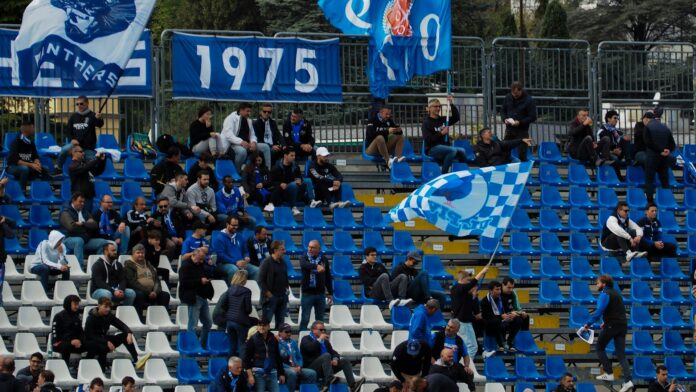 Fans waving blue flags at Stadio Giuseppe Sinigaglia in Como, illustrating the atmosphere of Italy’s lower leagues and the promotion journey to Serie A.