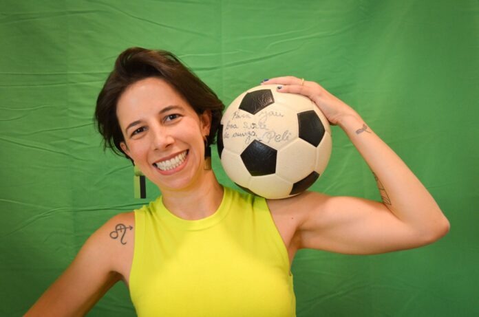 Mônica Esperidião smiling while holding a football signed by Pelé, representing her work in advancing women’s football.