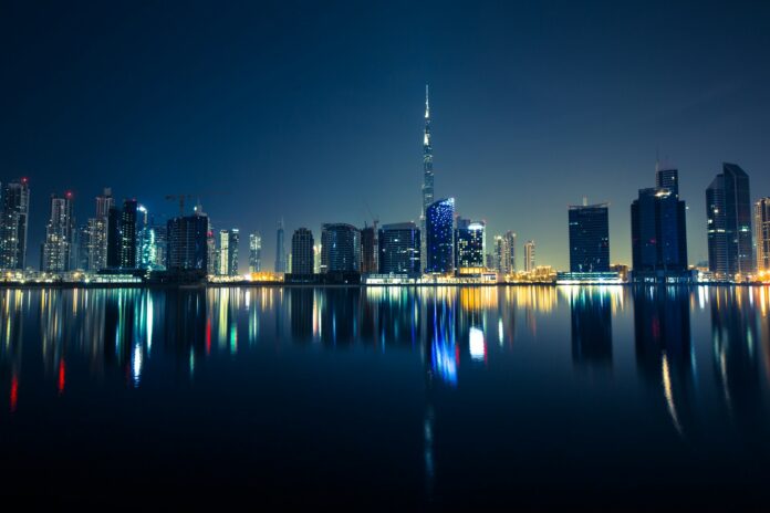 Dubai skyline at night with illuminated skyscrapers reflected on the water, representing the city’s booming real estate market and global investment appeal.