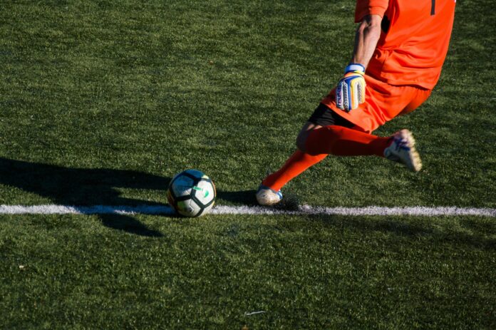 Goalkeeper in motion passing the ball during build-up play, highlighting modern offensive responsibilities in football.