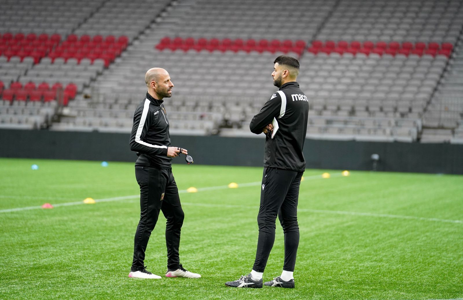 Jeyhan Bhindi discussing training details with a fellow coach on the pitch