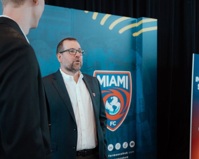 Mario Roitman, President of Miami FC, speaks at a club event in front of the team’s logo backdrop.
