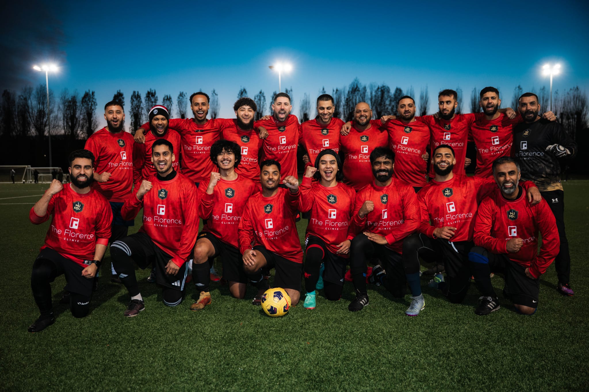 Football team in red kits from the Chelsea Muslim Cup tournament posing together on the pitch.