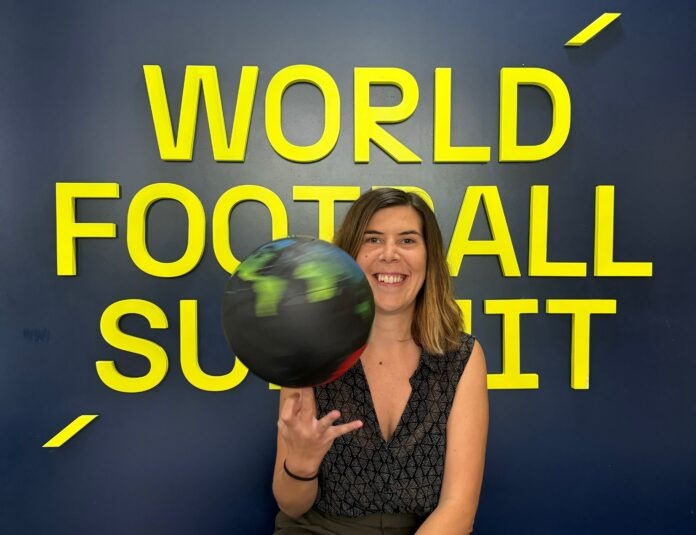 Arantxa Mandiola smiling in front of the World Football Summit backdrop while spinning a globe-themed football.