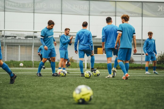 Football players in blue training kits practicing tactical drills on a synthetic pitch.