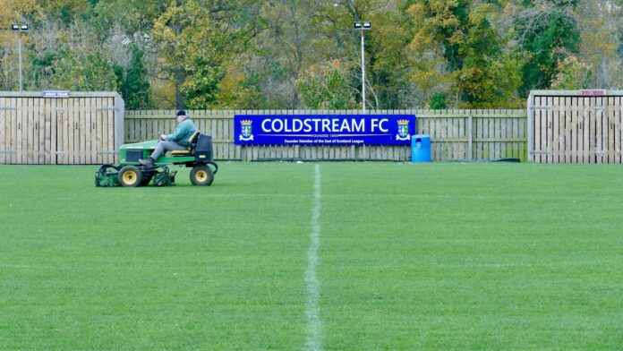Groundskeeper mowing the pitch at Coldstream FC, highlighting essential behind-the-scenes work in football.