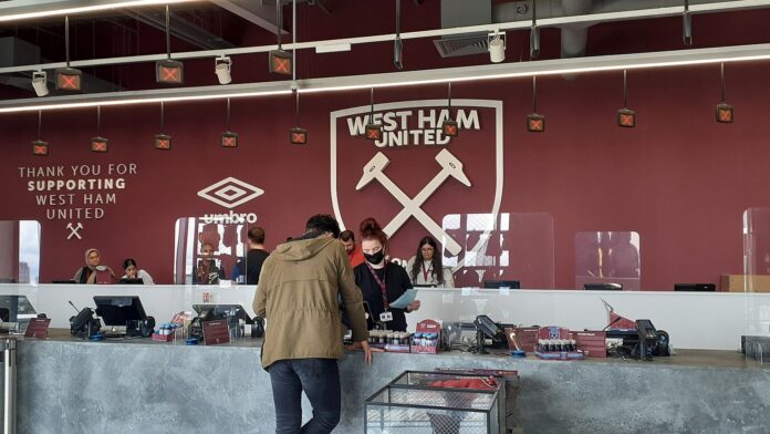West Ham stadium store with supporters browsing merchandise, highlighting the club’s working-class roots and industrial identity.