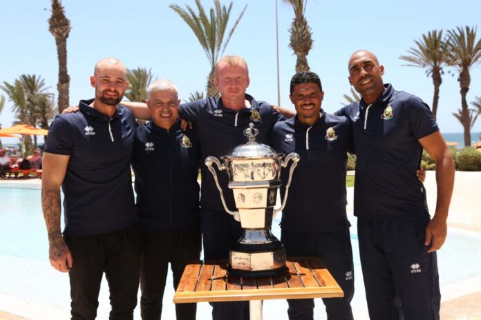 Yohwen Guihard with coaching team posing by the poolside with the league trophy.