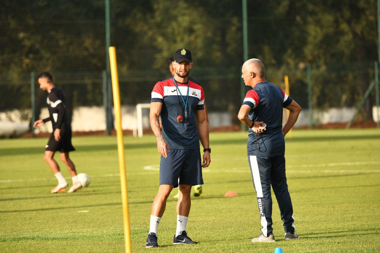 Yohwen Guihard coaching during a training session, speaking with his colleague on the pitch.