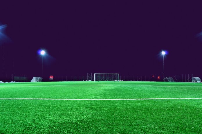 Brightly lit football pitch at night with empty goals and training equipment, creating a focused and modern development atmosphere.