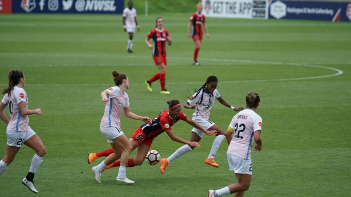 Women’s footballers contest possession during a match, highlighting professionalism and the pay gap discussed in the article.