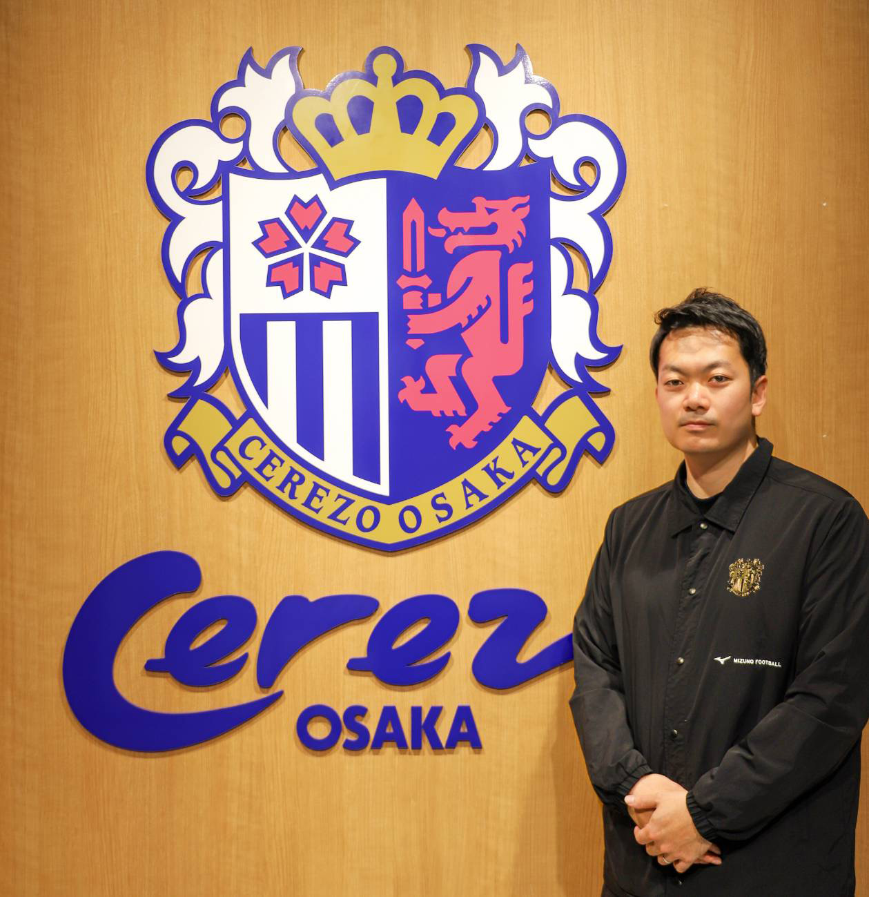 Shuya Ikuta of Cerezo Osaka stands beside club crest representing fan engagement and supporter culture strategy