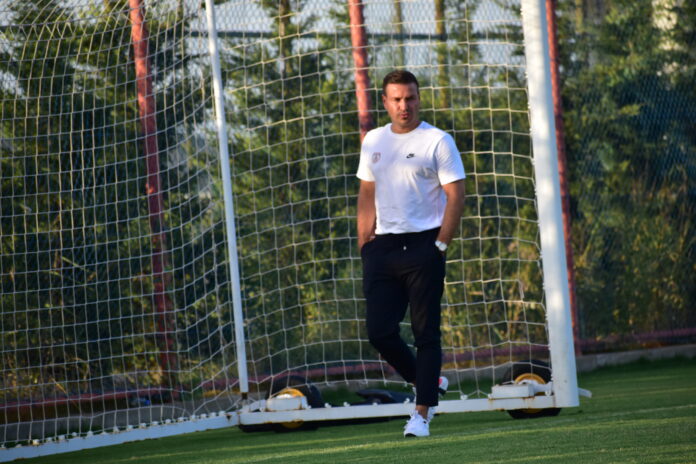 Murat Korkmaz walking beside a goal on a training pitch, reflecting his leadership role in football development.