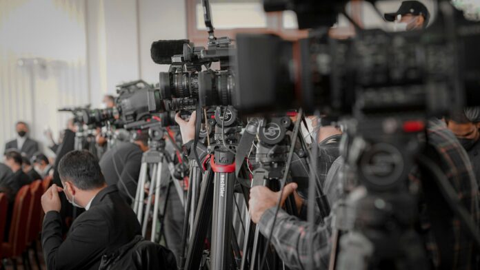 Professional video cameras filming a football press conference highlighting media scrutiny and public statements