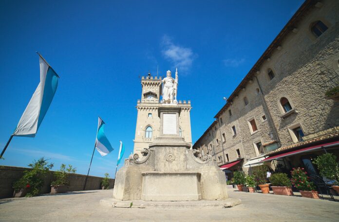 Statue of Liberty monument in Piazza della Libertà in San Marino with the Palazzo Pubblico and national flags in the background.