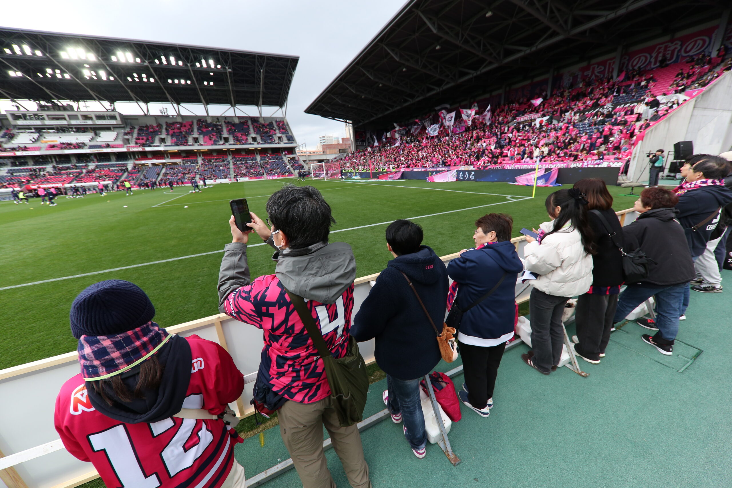 Fans watch Cerezo Osaka warm up from pitchside seats highlighting close connection between supporters and players