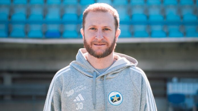 Jordi Ortola, Head of Scouting at Étoile Carouge FC, stands at a stadium highlighting his role in football recruitment