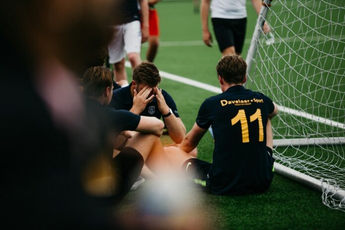 Young football players share a reflective moment beside the pitch during a training session.