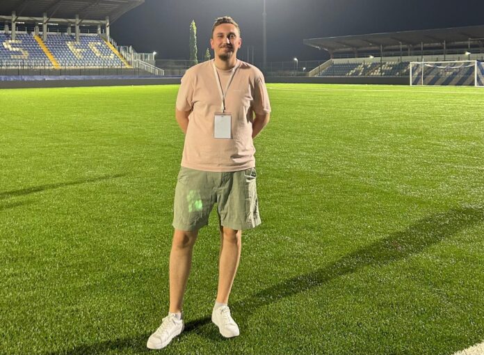 Football scouting professional on a floodlit pitch, reflecting Nordic talent identification and recruitment.
