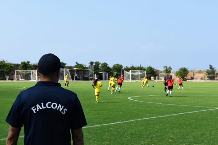 Scout observes a youth football match, reflecting player recruitment and talent evaluation.