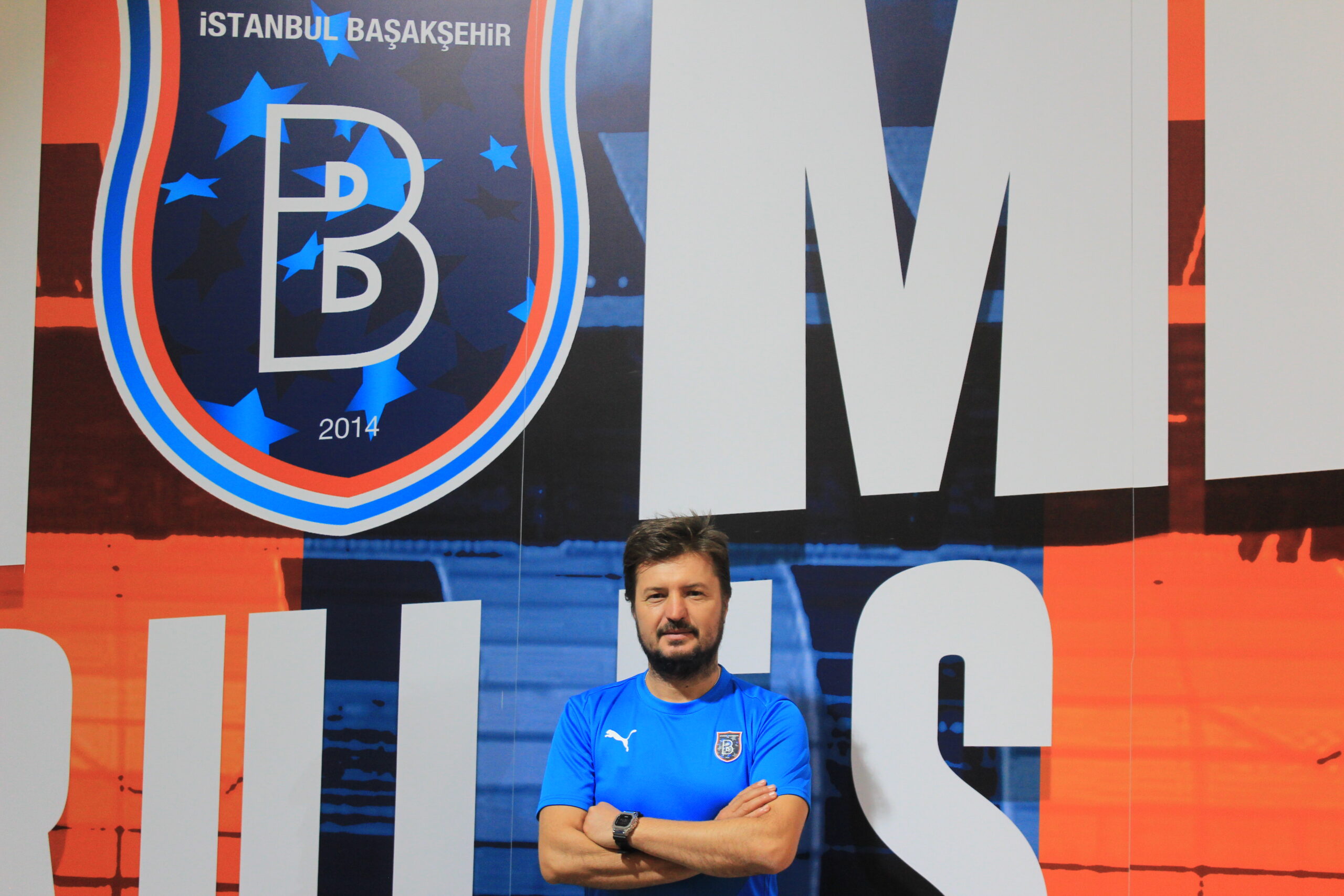 Ahmet Geçer standing in front of the İstanbul Başakşehir crest