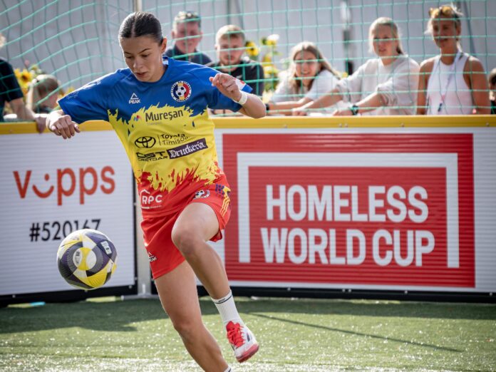 Romania player strikes the ball during a Homeless World Cup match with tournament branding in the background.