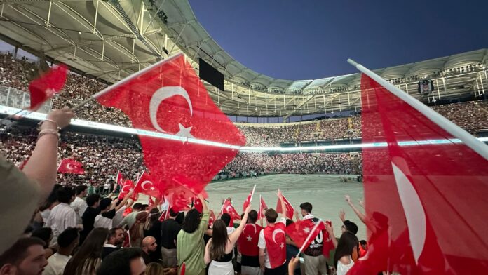 Türkiye supporters wave Turkish flags in a packed stadium during a national team match.