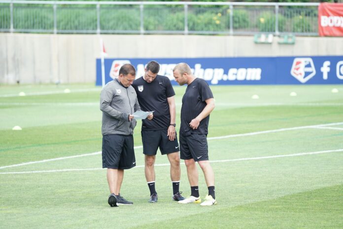 Football coaches discussing plans on a training pitch, reflecting the expertise and demands placed on coaching professionals.