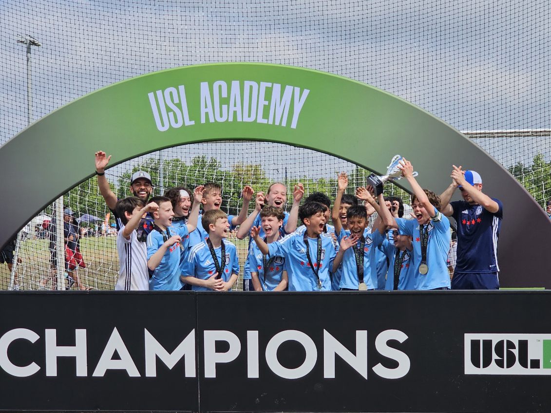 Chicago City youth players celebrate winning a USL Academy competition with coaches after lifting the trophy.