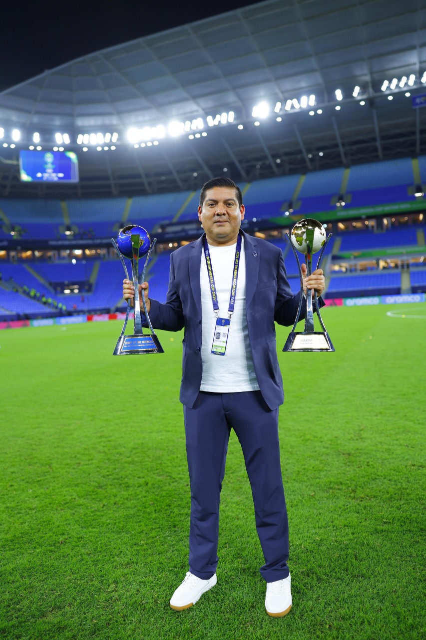 Vicente García Rodríguez holding two trophies on the pitch during Club Pachuca’s international success.
