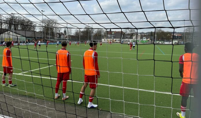 Youth football academy players wait beside the pitch, reflecting the pressures and uncertainty of player development.