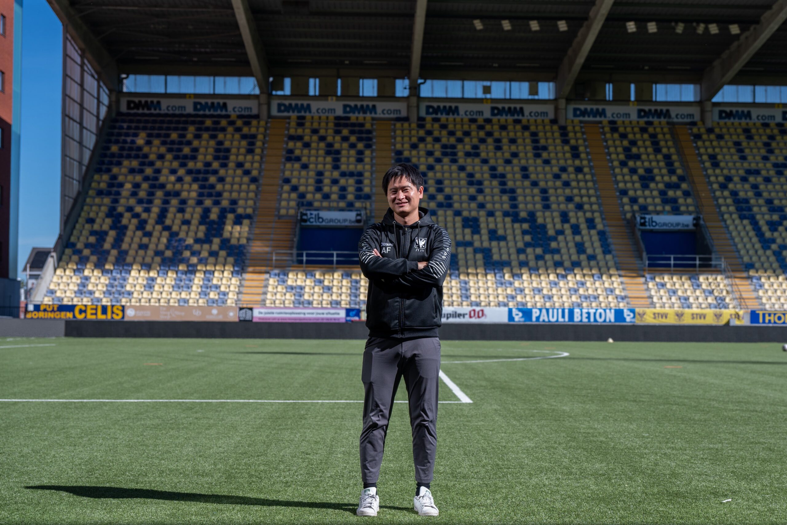 Akira Fukushima stands on the pitch at Sint Truiden VV’s stadium with his arms folded.