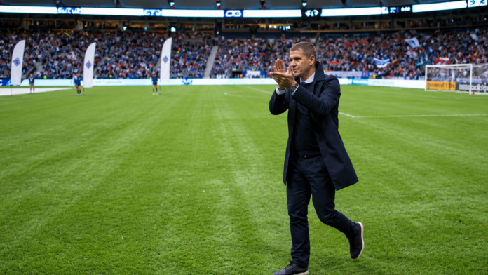 Carl Robinson applauds supporters on the football pitch in front of a packed stadium.