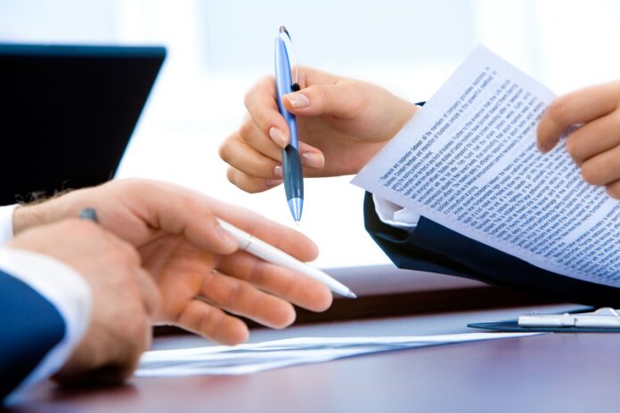 Football executives review contract documents during negotiations related to an MLS trade.