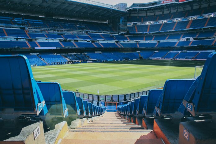 Empty football stadium in Madrid with rows of blue seats, a central aisle and the pitch beyond.