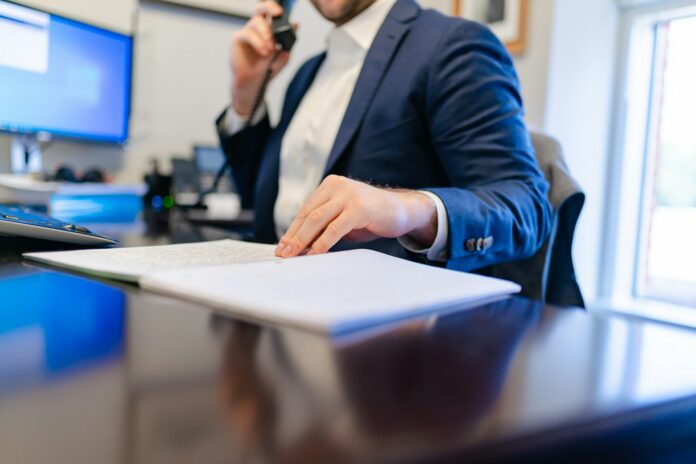 A football executive reviews documents while speaking on the phone, representing the Chief Soccer Officer role in MLS.