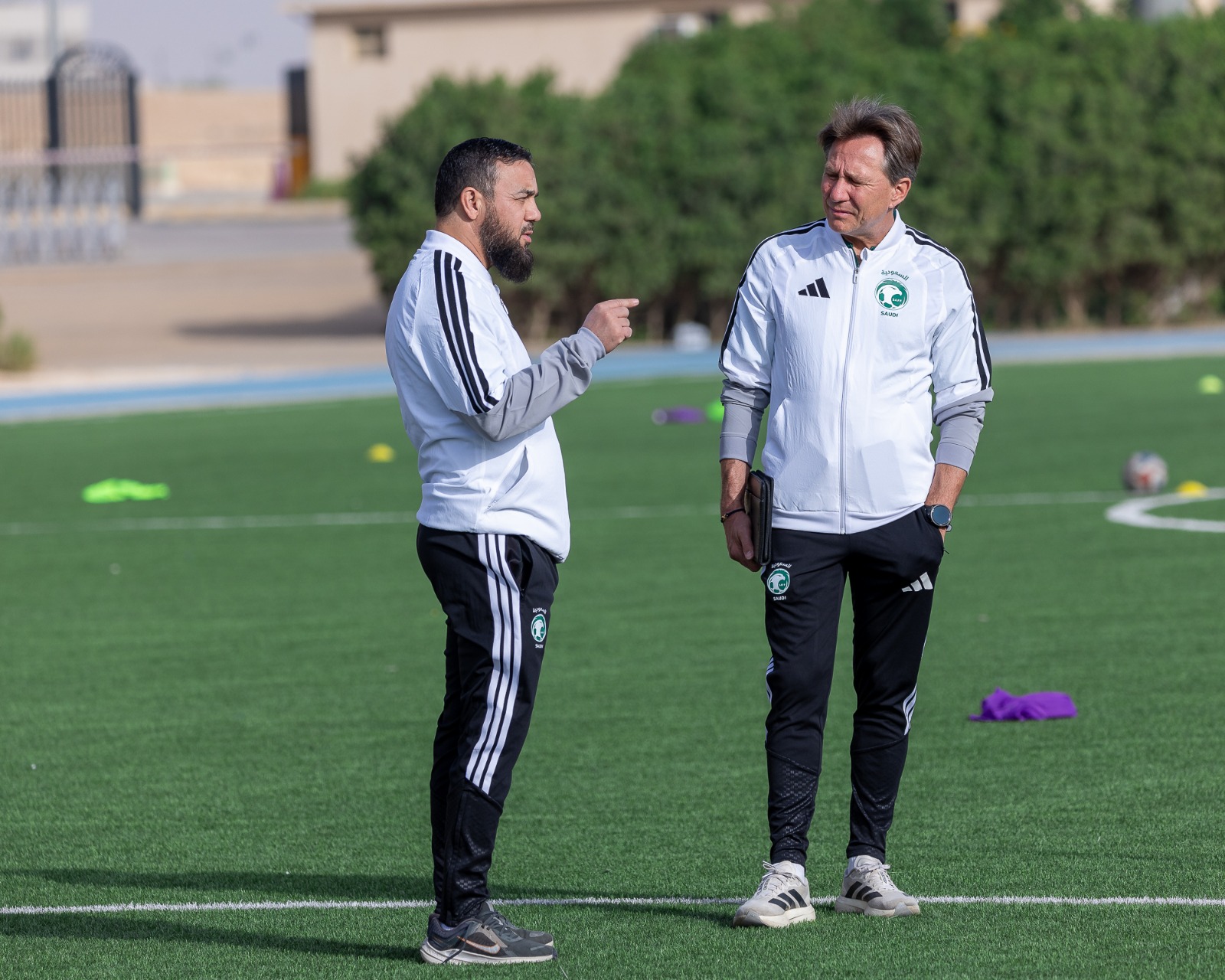 Franck Thivilier échange avec un membre du staff de la Fédération saoudienne de football sur le terrain.